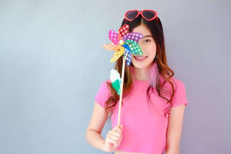 Portrait beautiful asian teen girl wearing pink dress on gray background, fashion summer set with colorful wind turbine or pinwheel or wind toy holding in hand,  emotions action, happy life conceptの写真素材