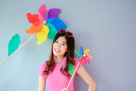 Portrait beautiful asian teen girl wearing pink dress on gray background, fashion summer set with colorful wind turbine or pinwheel or wind toy holding in hand,  emotions action, happy life conceptの写真素材