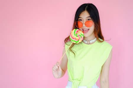 Portrait beautiful asian teen girl beaming smile on pink background, fashion summer set with colorful lollipop candy holding in hand,  emotions action, happy life conceptの写真素材