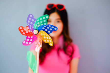 Portrait beautiful asian teen girl wearing pink dress on gray background, fashion summer set with colorful wind turbine or pinwheel or wind toy holding in hand,  emotions action, happy life conceptの写真素材