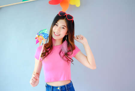 Portrait beautiful asian teen girl wearing pink dress on gray background, fashion summer set with colorful wind turbine or pinwheel or wind toy holding in hand,  emotions action, happy life conceptの写真素材