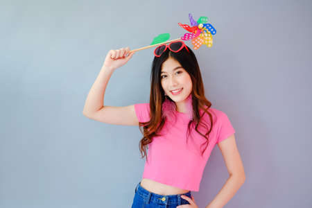 Portrait beautiful asian teen girl wearing pink dress on gray background, fashion summer set with colorful wind turbine or pinwheel or wind toy holding in hand,  emotions action, happy life conceptの写真素材