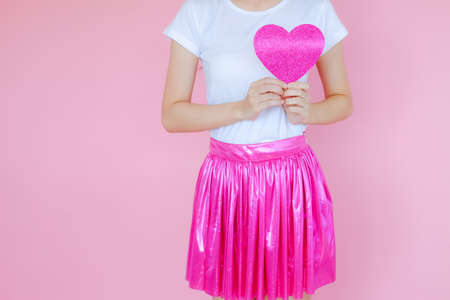Portrait beautiful asian teen girl wearing white T-shirt and pink skirt on pink background, happy valentine day in love concept, model holding red heart sign in handの写真素材