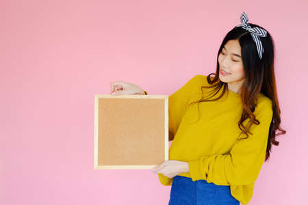 Portrait beautiful asian cheerful girl beaming smile on pink background, woman in casual clothes holding cork board, emotions action, fashion setの写真素材