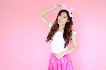 Portrait beautiful asian woman wearing white T-shirt and pink skirt on pink background, happy valentine day in love concept, emotions action, happy summer life with pink bow headbandの写真素材