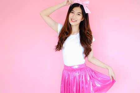 Portrait beautiful asian woman wearing white T-shirt and pink skirt on pink background, happy valentine day in love concept, emotions action, happy summer life with pink bow headbandの写真素材