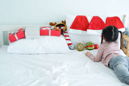 little child girl playing decorative gifts and red Santa Claus hat and gift boxes or present lying on the bed, holiday in festive Merry Christmas or Xmas and happy new year conceptの写真素材