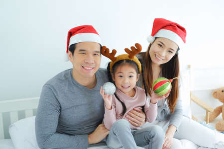 Asian family celebrating Christmas wearing red Santa Claus hat with decorative gifts and gift boxes or present in bedroom, holiday in festive Merry Christmas or X'mas and happy new year conceptの写真素材