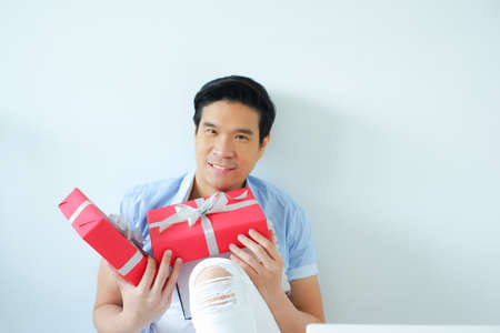 posing asian handsome man smiling with red gift box holding in hand, happiness in festive Christmas or X mas and happy new year or Happy Birthday conceptの写真素材