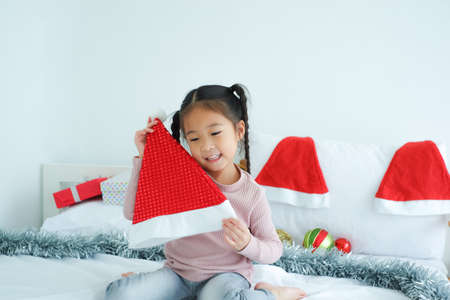 little child girl playing decorative gifts and red Santa Claus hat and gift boxes or present lying on the bed, holiday in festive Merry Christmas or Xmas and happy new year conceptの写真素材