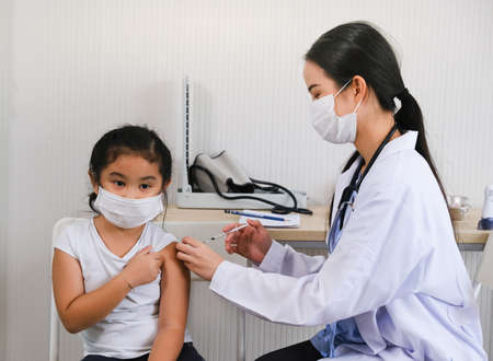 Asian doctor woman or nurse giving flu or antiviral vaccine to little asia child girl in hospital or clinicの写真素材