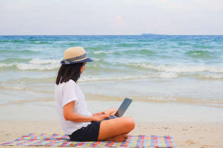 Young asian woman playing laptop computer on tropical beachの写真素材