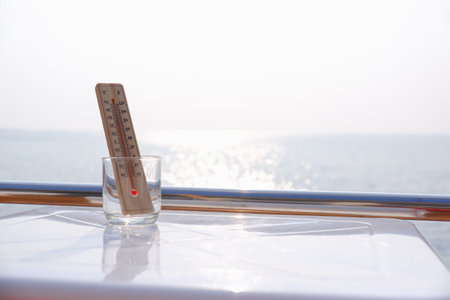 thermometer in a glass on white table view sea background, global warming concept