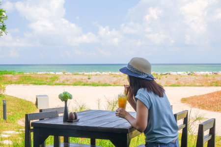 Asia woman drinking orange juice on table near tropical seasideの写真素材