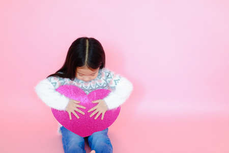Portrait beautiful cute asian child girl on pink background with red heart sign, valentine day in love conceptの写真素材
