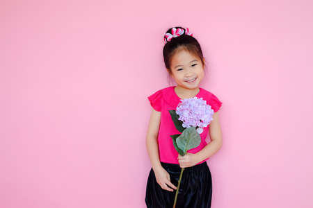 Little cute asian small girl on pink background with flower bouquetの写真素材