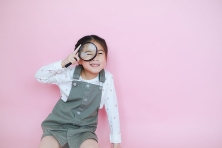 Portrait beautiful cute asia child girl on pink background playing magnifying glass