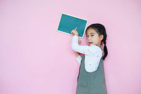 Portrait beautiful cute asian child girl on pink background with drawing board holding in handの写真素材