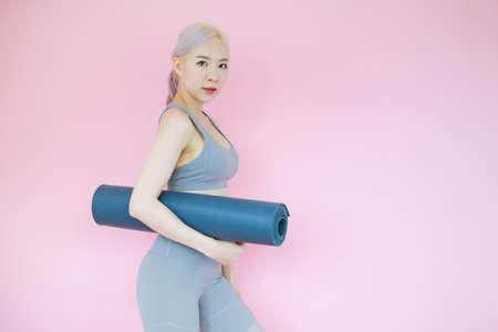 beautiful asian woman on pink background with mat yoga, fitness sports and recreation conceptの写真素材