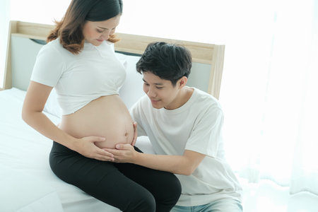 portrait asian young pregnant woman and husband happy together on the bedの写真素材