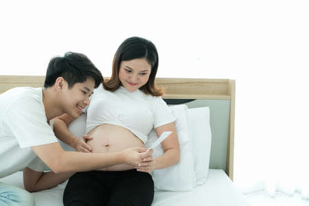 portrait asian young pregnant woman and husband happy together on the bedの写真素材