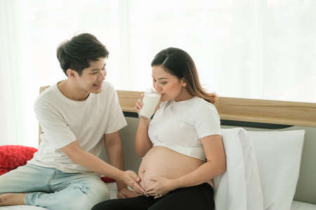 Asia man take care pregnant woman and drinking milkの写真素材