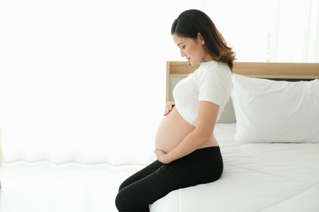 portrait asian young pregnant woman sit on the bed with hand on belly