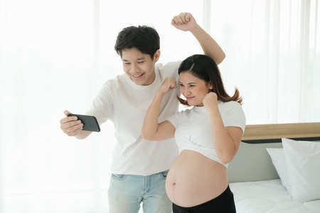 portrait asian pregnant woman and husband happy together with smart phoneの写真素材