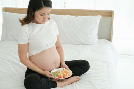 Asian husband take care pregnant wife and eat mixed fruitsの写真素材