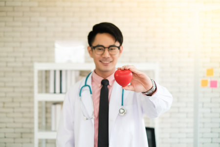 asia doctor man dressed in white gown with stethoscope holding heart in hand