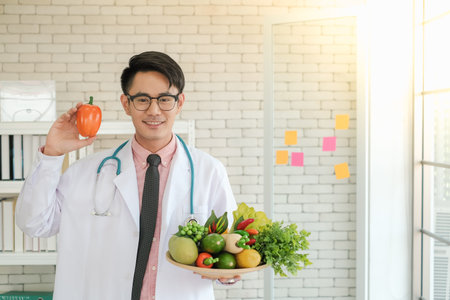 Professional nutritionist asian man holding fresh vegetables in clinic roomの写真素材