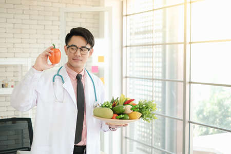 Professional nutritionist asian man holding fresh vegetables in clinic roomの写真素材