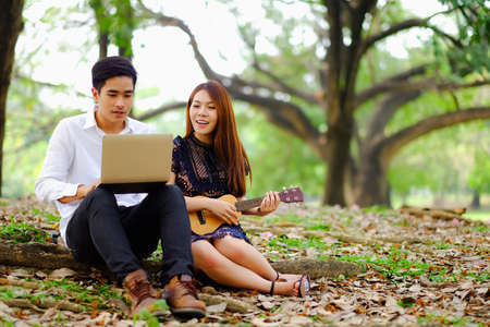 Portrait asian young couple in love, boyfriend and girlfriend happy in park playing social network or social media on notebook or laptop onlineの写真素材