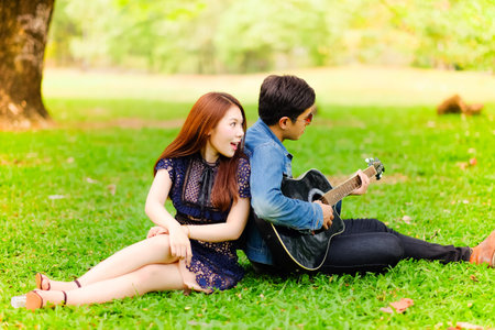 Portrait asian young couple in love, boyfriend and girlfriend playing guitar in park happy summer...