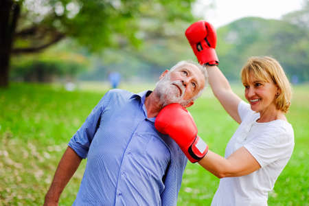 Portrait caucasian senior woman and old man, couple elderly fighting each other with boxing red gloves in parkの写真素材