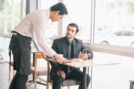 asian waiter serving caucasian businessman in cafe or restaurantの写真素材
