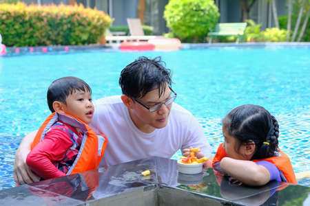 happy asian single dad with son and daughter playing in swimming poolの写真素材