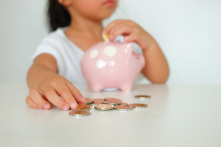 close up hand little cute girl putting coin to piggy bank
