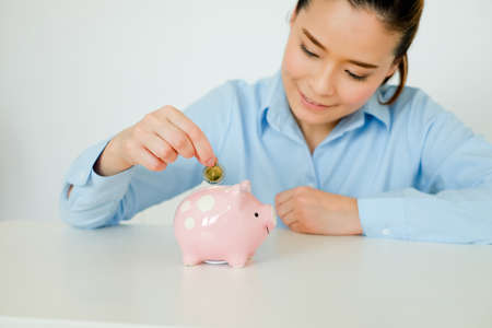 Asian woman putting coin to piggy bank on tableの写真素材