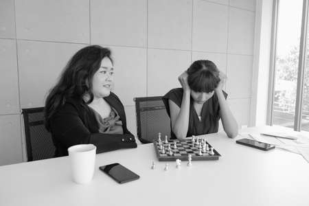 two asian employee women playing chess in work spaceの写真素材