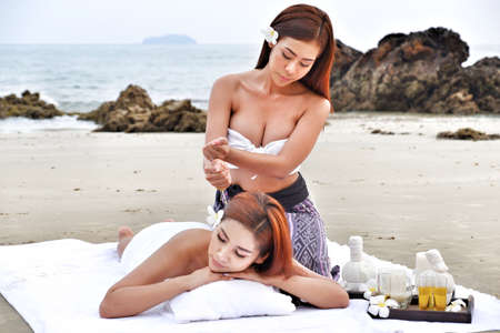 two asian sexy women doing spa massage together on the tropical beachの写真素材