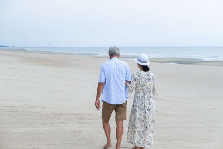 Portrait asian senior woman and caucasian old man relaxing together on the beachの写真素材