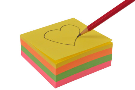 Pencil drawing heart on a yellow paper isolated on white.(focus is on the point of the pencil)