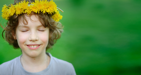 Handsome boy with a wreath of yellow dandelions on his head closed his eyes, breathing warm air summer.の写真素材