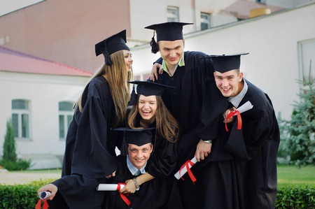 The group of students embracing looking at the camera. They have degrees in their hands. Friends having fun laughingの写真素材