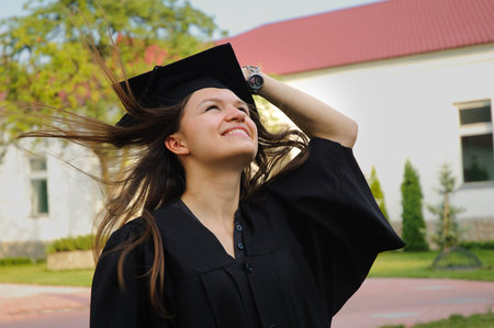 Smiling student looks up at the sky. She holds a headdress. Her hair fluttering in the wind.の写真素材