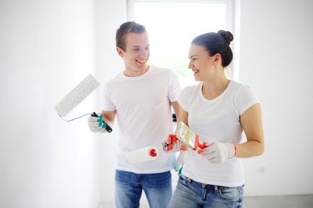 The guy and the girl in jeans and white T-shirts laugh. In the hands of a guy roll. A girl holding a roller and brushの写真素材