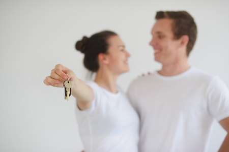 Man and woman in white shirts Stoyan embracing against a white wall. They are happy. Girl holds in his hand the keysの写真素材