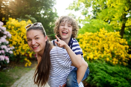 Young woman playing with boy 8-9 years against a background of flowering garden. They are very funの写真素材