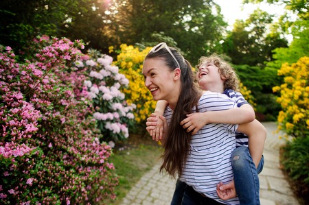 Boy 8-9 years old on the shoulders of a young woman. Both are fun to laugh. They play in a densely flowered garden.の写真素材
